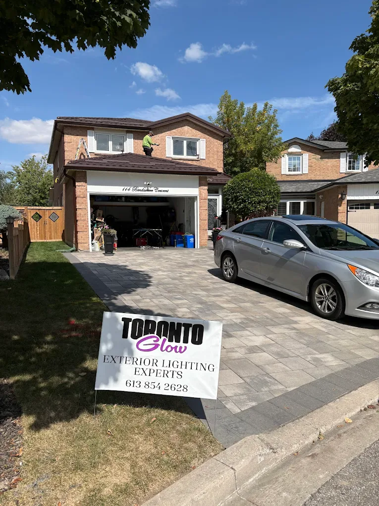 Toronto Glow yard sign on a GTA lawn with an installer on the roof mounting permanent lighting