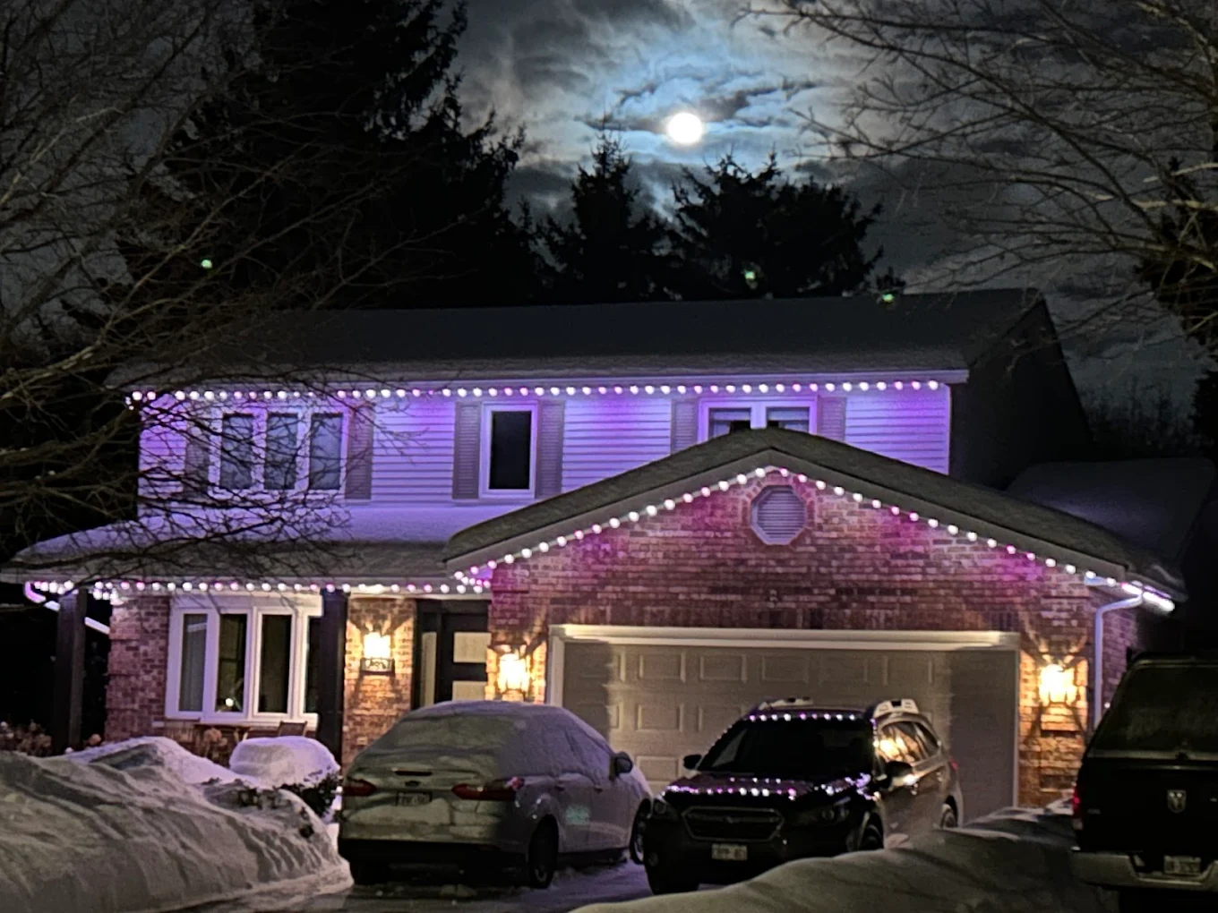 GTA home glowing with purple and white permanent Christmas lights under a full moon during a snowy Ontario winter night.