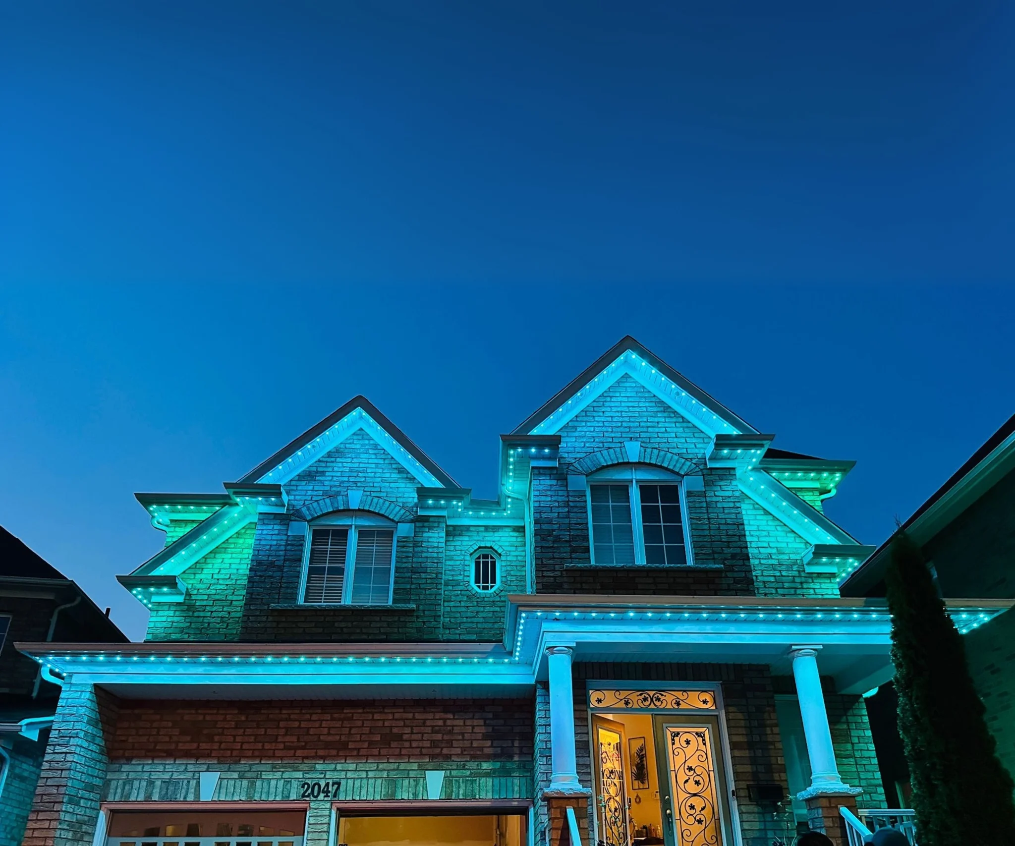 GTA brick home illuminated with blue and teal permanent holiday lights along the roofline