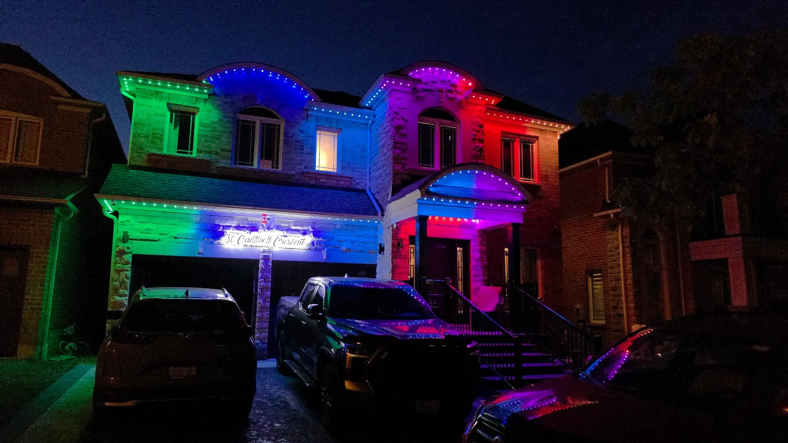 GTA home displaying green, blue, red and purple permanent outdoor LED lights across two rooflines and the front porch, installed by Toronto Glow