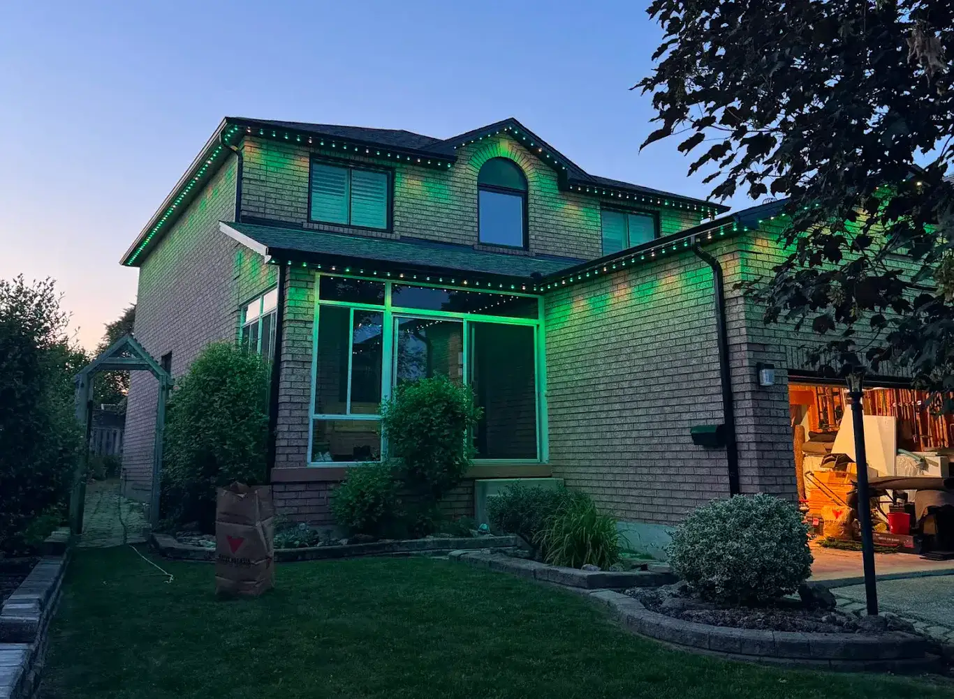 Green permanent outdoor LED lights covering the full roofline and soffits of a two-storey brick GTA home at dusk, viewed from the backyard — installed by Toronto Glow