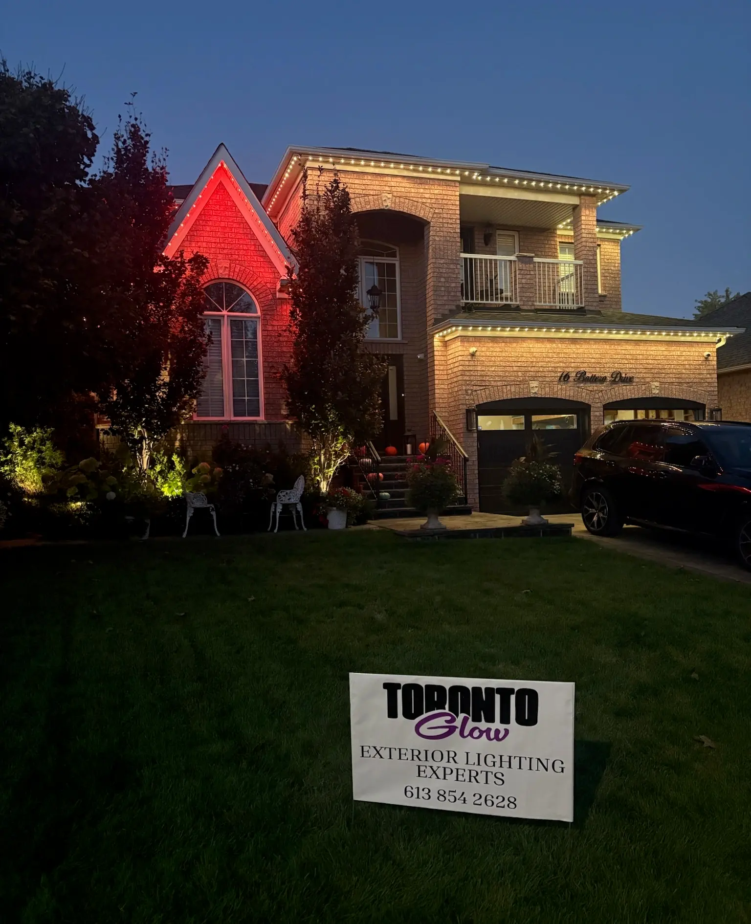 GTA home lit with red permanent Christmas lights by Toronto Glow — warm white roofline accents, landscape lighting, and Toronto Glow yard sign in the foreground.