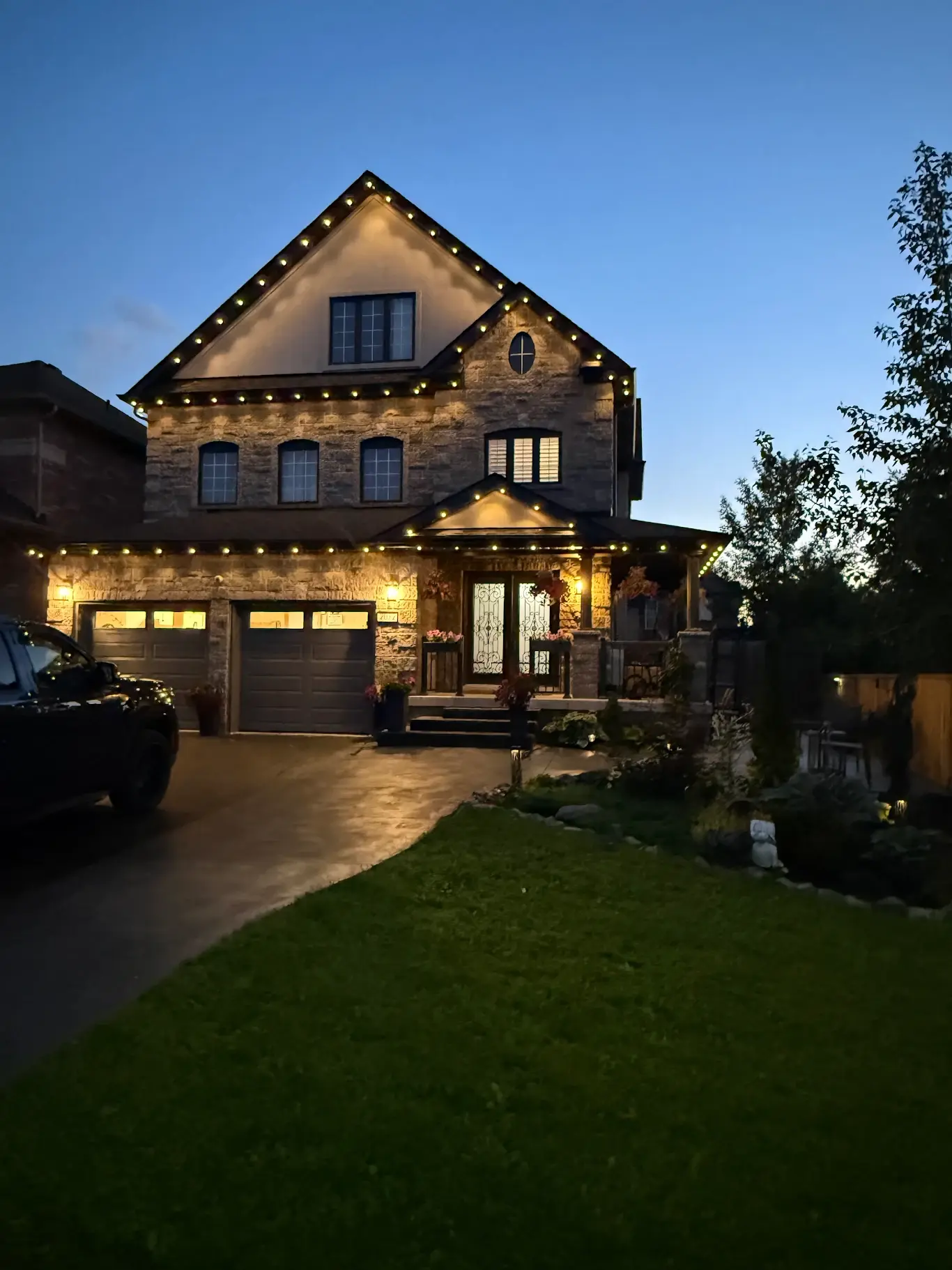 GTA stone home with warm white permanent LED roofline lighting at dusk
