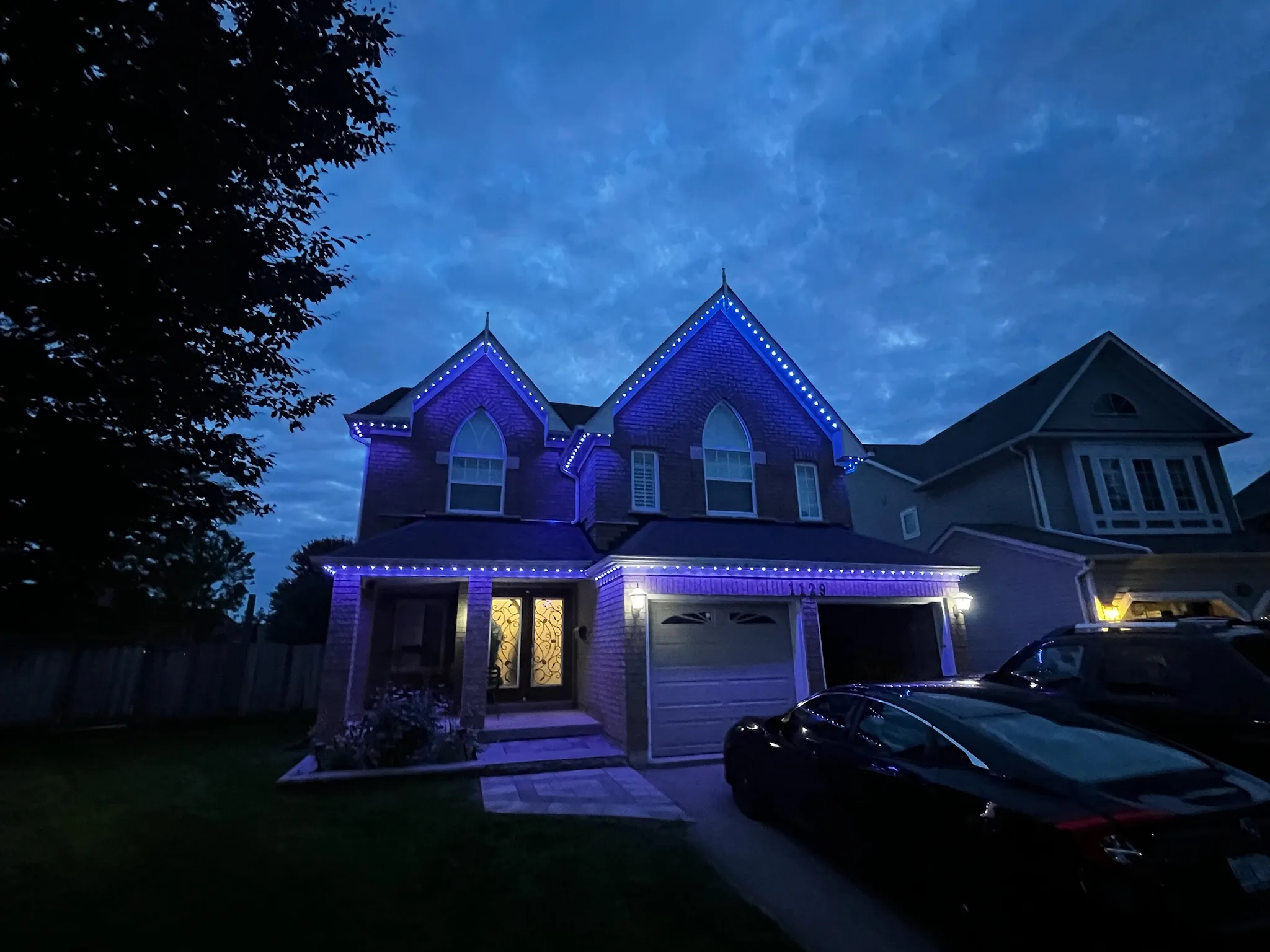 Stone GTA home with warm gold permanent Christmas lights by Toronto Glow glowing along the roofline and peaks at dusk.