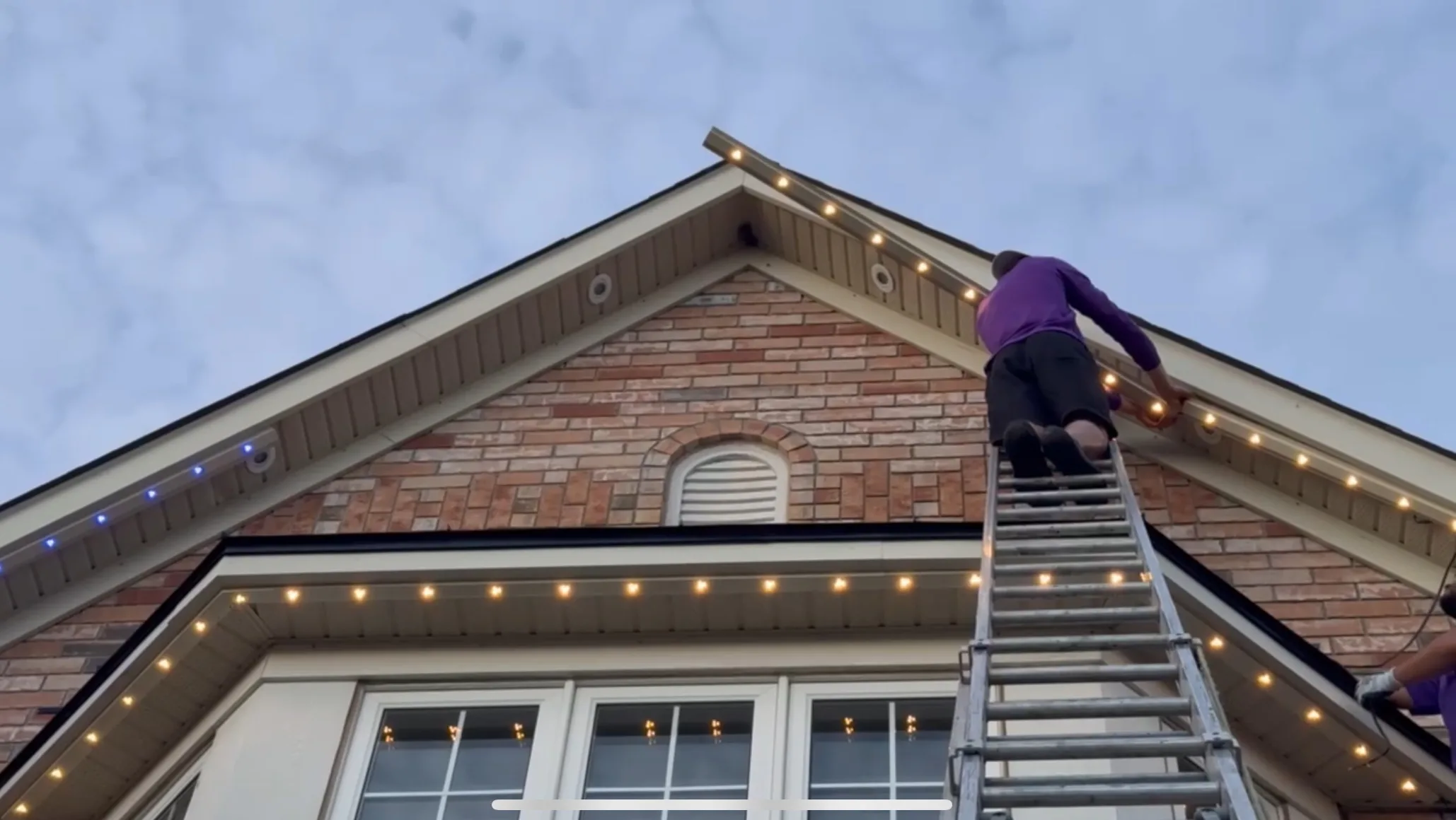 Toronto Glow installer on ladder mounting permanent LED lighting on a brick home at dusk