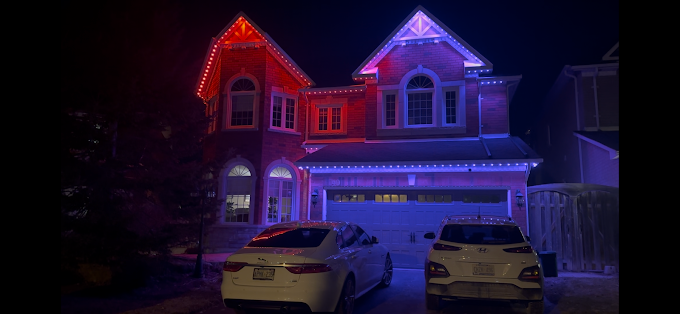GTA home lit with red and blue permanent Christmas lights across the roofline, soffits, and garage at night.